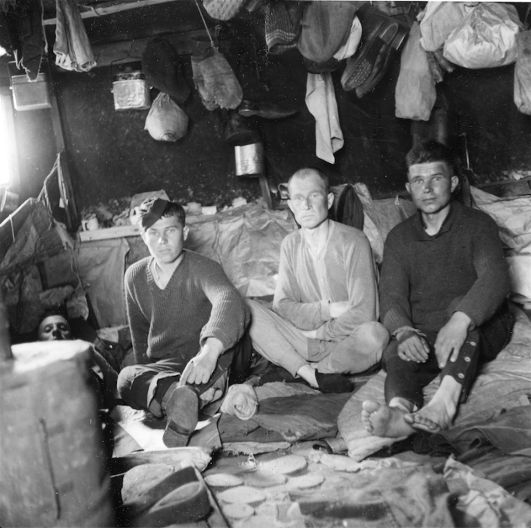 Sorthvitt bildet av fire fanger som sitter tett sammen inni teltet